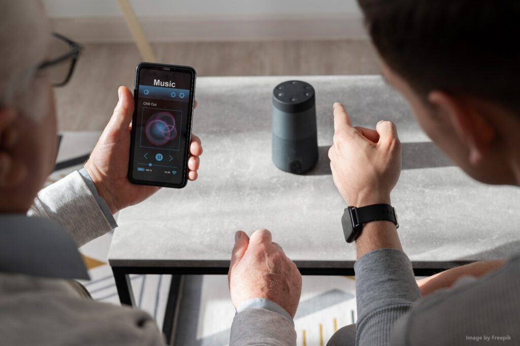 Image of 2 people looking at a smart speaker while holding a phone
