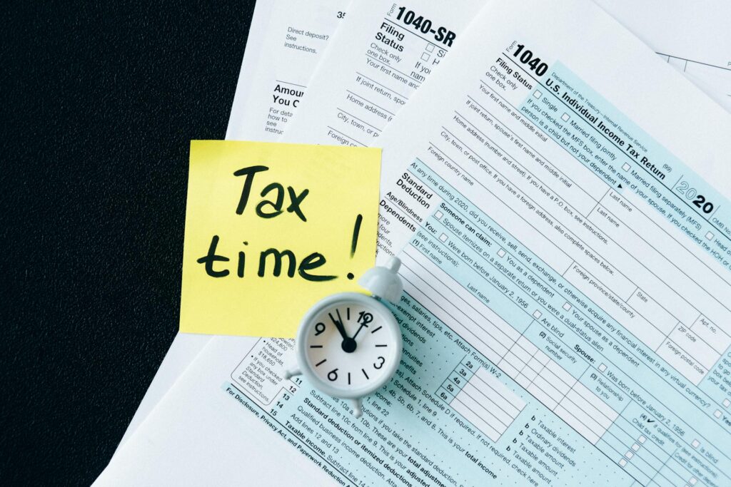 Tax documents, a sticky note that says 'Tax time!', and a small clock symbolize the urgency of tax season—highlighting growing concerns around AI-driven tax fraud, where advanced technology is used to exploit filing systems and impersonate taxpayers