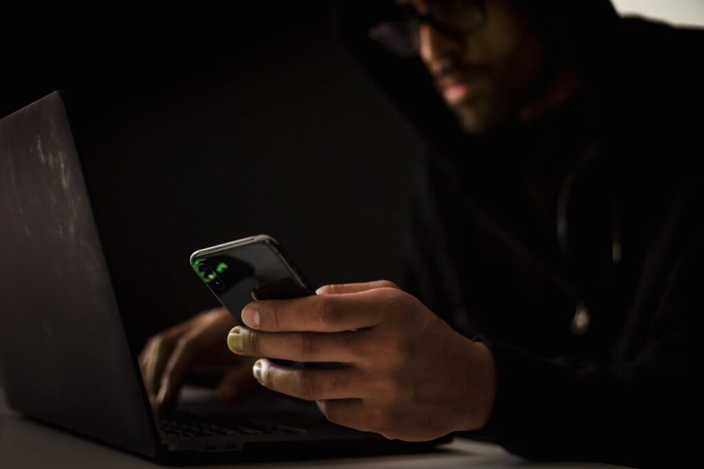 image of man in shady room, with phone performing digital kidnapping.